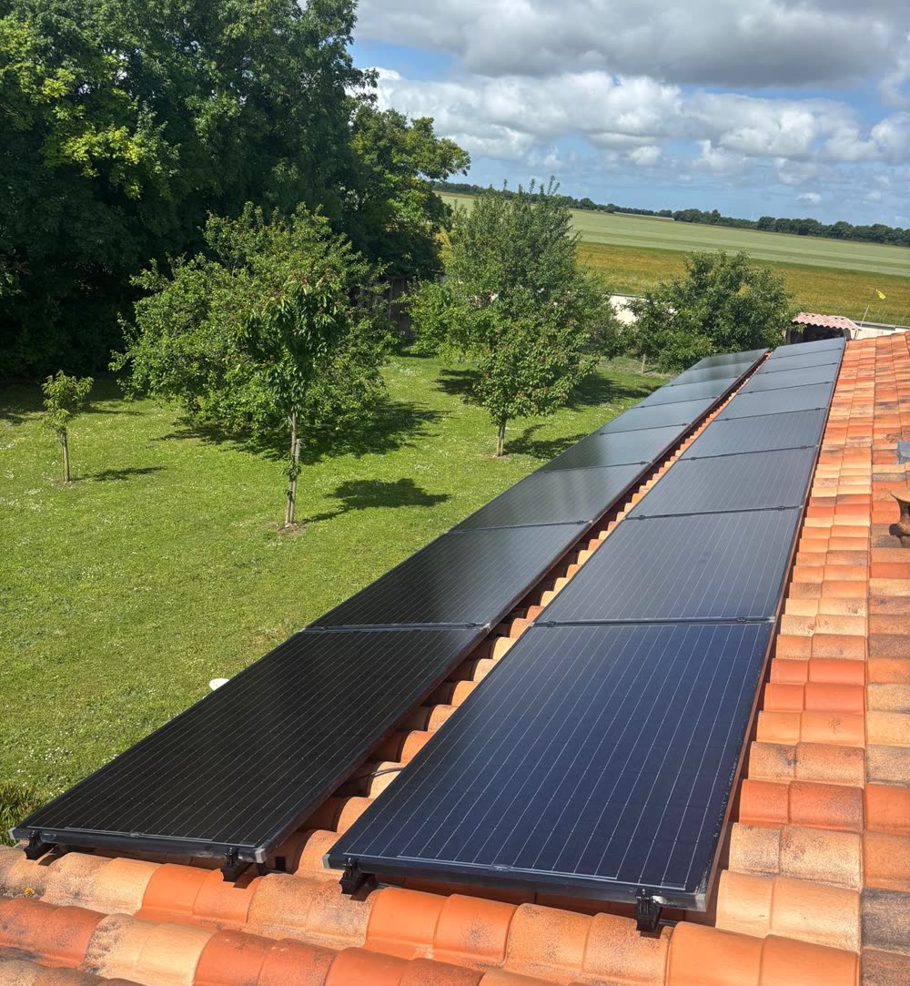 Deux rangées de panneaux sur une toiture en tuiles, en bordure de verger