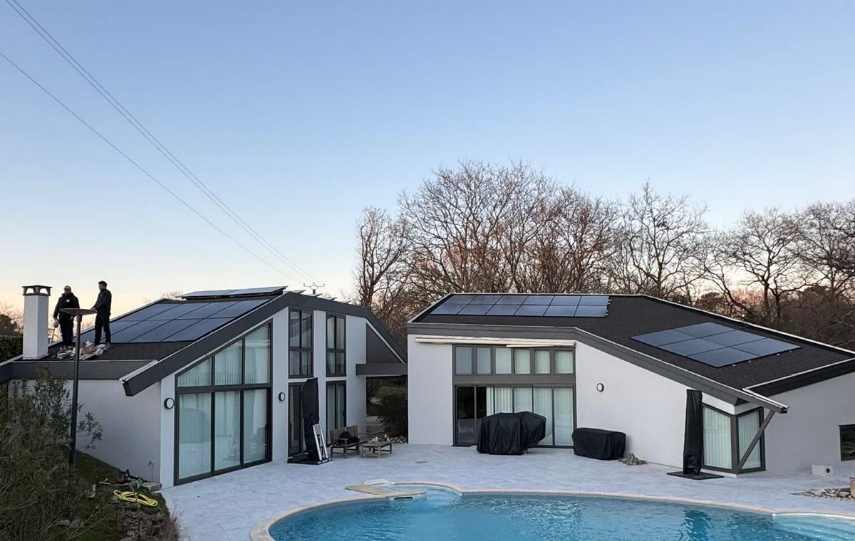 Villa contemporaine équipée de panneaux solaires sur ses deux toitures, deux techniciens sur le toit